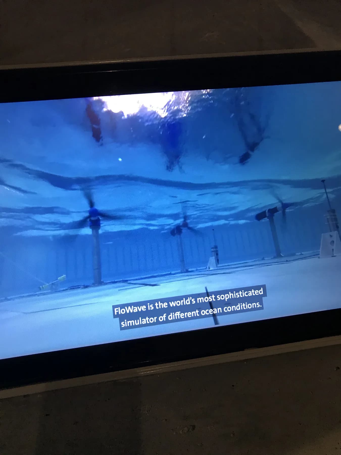 A V&A Dundee video display showing the FloWave ocean simulator with subtitles.